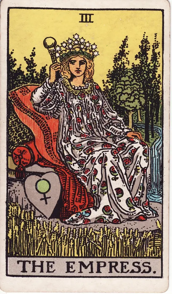 The Empress tarot card from the Rider-Waite-Smith deck: a crowned woman reclining on cushions in a field of ripe wheat, a shield bearing the sign of Venus beside her.