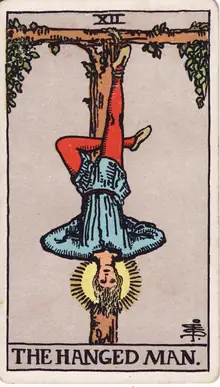 The Hanged Man tarot card from the Rider-Waite-Smith deck: a man suspended by one ankle from a living T-shaped tree, a halo of light around his head.