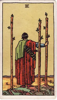 Three of Wands tarot card from the Rider-Waite-Smith deck: a figure on a cliff watching ships sail out, three staves planted around him.