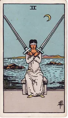Two of Swords tarot card from the Rider-Waite-Smith deck: a blindfolded woman seated at the shore holding two crossed swords.