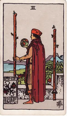 Two of Wands tarot card from the Rider-Waite-Smith deck: a man on a castle rampart holding a globe, one staff fixed to the wall and one in his hand.