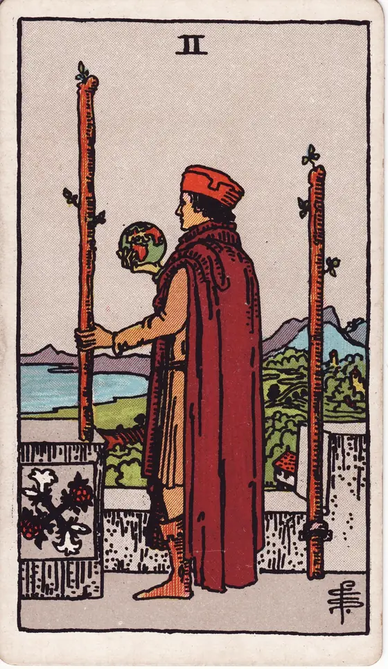 Two of Wands tarot card from the Rider-Waite-Smith deck: a man on a castle rampart holding a globe, one staff fixed to the wall and one in his hand.