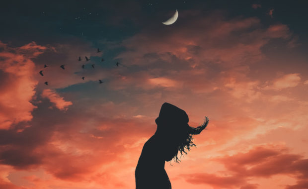 Woman standing in front of sunset with crescent moon in the sky