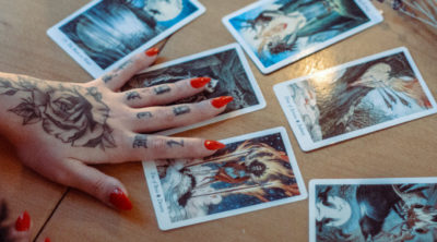 girl with red nails and tattoos on her hand holding a 6-card tarot spread on the table