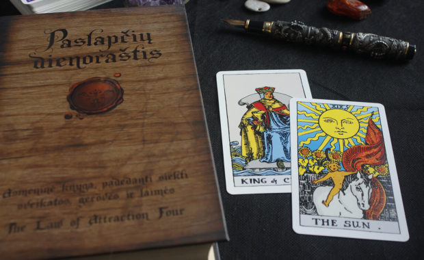 the sun tarot card sitting on a table with another card and a book titled the law of attraction four