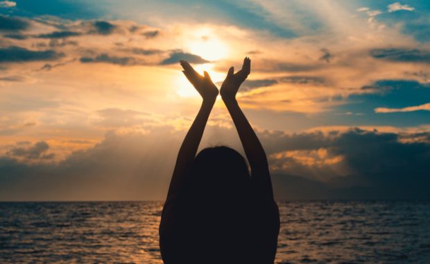 Woman raising hands at sunset